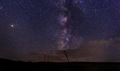Silhouette of a pillar and electric wires on the background of the milky way