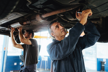 Mechanics fixing car exhaust system in garage