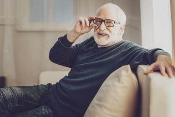 Wonderful mood. Cheerful joyful man smiling while fixing his glasses