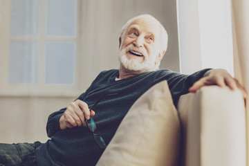 Pleasurable time. Joyful senior man smiling while enjoying his rest at home - obrazy, fototapety, plakaty
