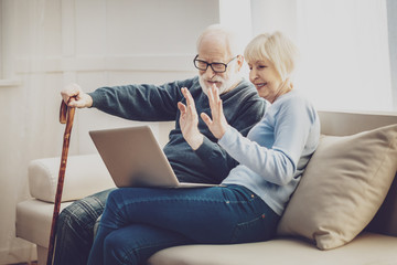 Progressive pensioners. Nice elderly people greeting their grandchildren while having a video call