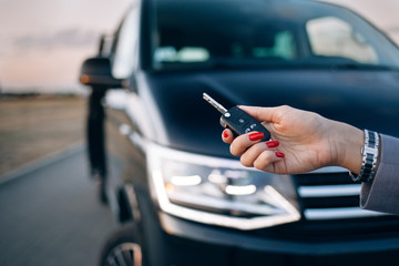 Woman is holding car keys in front of minivan - obrazy, fototapety, plakaty