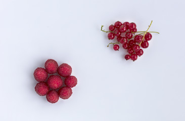 Raspberries and red currants are located diagonally on a light background