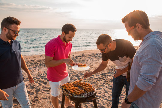 Happy friends are having fun while they are preparing a barbecue on the beach. Vacation concept.