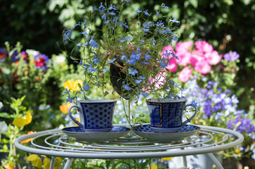 Blue mood: two blue cups and a blue flower are on a table in a beautiful garden.