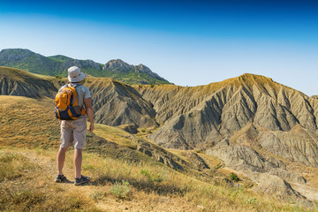 Man hiker with backpack standing against badland