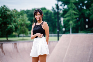 Obraz premium A portrait of a sporty, young Asian Chinese teenager skater girl at the skate park during the day. She is smiling gracefully and playfully as she whirls and twirls in front of the camera.