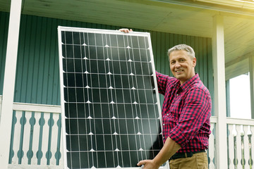 Solar panels in the hands of men . Energy production technologies. Wooden house background.