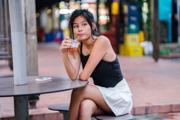 An image of a young and pretty Chinese Asian at the hawker center taking a sip from her cold...