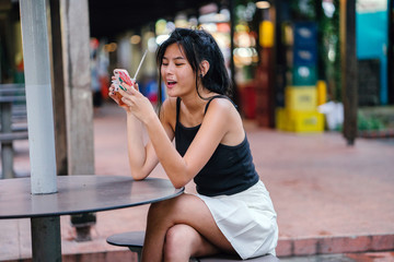 A young woman at the hawker center sitting and enjoying her cold drink while resting. She is...