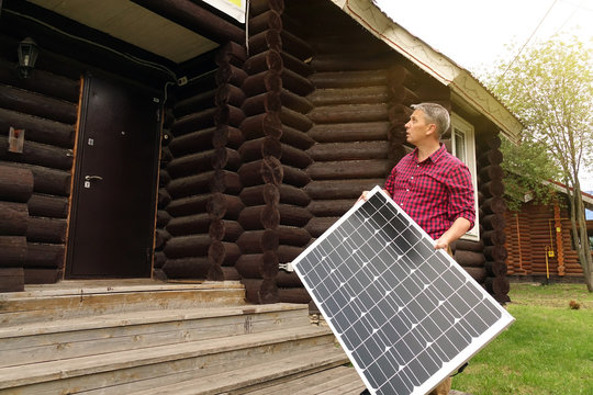 Solar panels in the hands of men . Energy production technologies. Wooden house background.