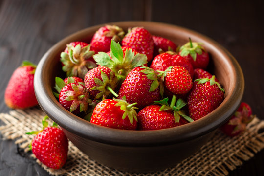 Fresh strawberries in ceramic bowl on dark wooden background
