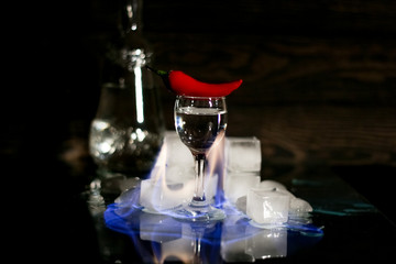 a shot of vodka, an alcoholic beverage, next to ice, fire, ice, red chili pepper. The concept of alcohol, spirits