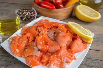 Raw pickled trout fillet and salmon pieces in a white plate. Wooden background.