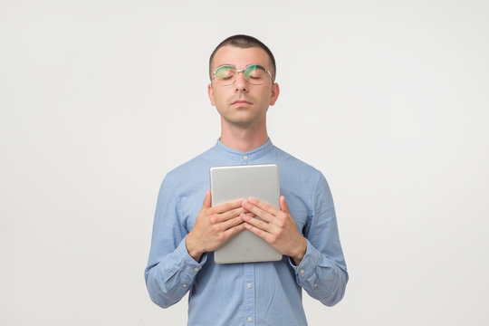 Young handsome hispanic man in glasses standing with closed eyes holding tablet device