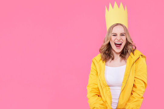 Beautiful teenage girl in bright yellow jacket and party hat shouting with excitement. Attractive cool young woman fashion portrait over pastel pink background.
