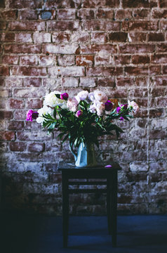 Peony flowers at vintage chair in loft interior, copy space on brick wall