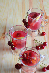 Fruit juice cocktails in three glass cups with red cherries on natural wooden table background. Summer drink.