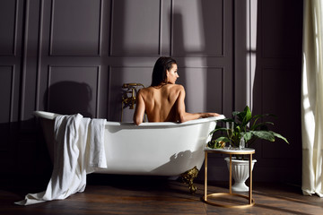Young beautiful woman sitting in bathroom near expensive bathtub bath looking at the corner on dark 
