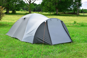 Tent on meadow with green trees on background in sunny summer day with copy space for text on grass. Traveling and hiking concept.