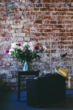 Loft interior with bunch of peony flowers, retro suitcase  and straw hat, copy space on brick wall