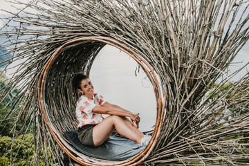 Young tourist enjoying her travel around Bali island , Indonesia. Making a stop on a beautiful hill overlooking a large lake. Photographs in a straw nest, natural environment. Lifestyle.