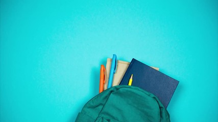 Turquoise backpack with colored school supplies sticking out of it.