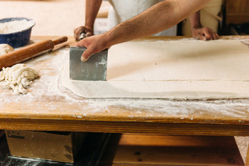 Baker is cutting and kneading dough to prepare traditional bread on a rustic table in a bakery. Bakery Concept.