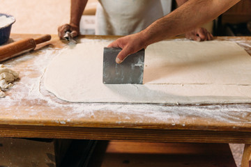 Fototapeta na wymiar Baker is cutting and kneading dough to prepare traditional bread on a rustic table in a bakery. Bakery Concept.