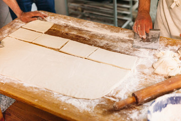Baker is cutting and kneading dough to prepare traditional bread on a rustic table in a bakery. Bakery Concept.