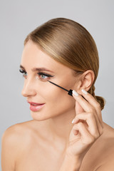 Fototapeta premium Portrait of beautiful blonde woman applying liquid eyeliner with brush. Natural make up. Beauty woman with perfect skin. Makeup concept.