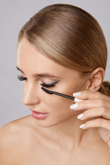 Portrait of beautiful blonde woman applying mascara with brush. Natural make up.Long lashes. Beauty woman with perfect skin. Makeup concept.