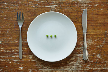 three single peas on plate knife and fork inadequate nutrition