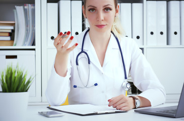 Young female doctor sitting at the table and working at hospital office. Health care, insurance and help concept. Physician ready to examine patient