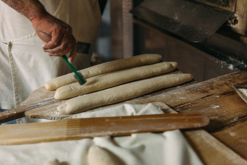 Baker is preparing the raw dough bread before baking in a wood oven. Traditional Bakery Concept.