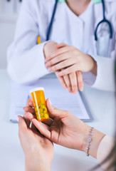 Female medicine doctor hand hold jar of pills and explain how to take pills to patient at worktable. Panacea and life save prescribing treatment legal drug store concept.