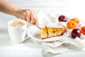 Homemade cake.Food preparation.fruit sweet cake with apricots and plums. Female hand breaking off a piece of cake with a fork