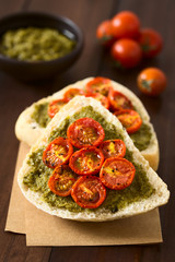 Olive bread roll halves spread with basil pesto and topped with roasted cherry tomato halves, photographed on dark wood with natural light (Selective Focus, Focus one third into the image)