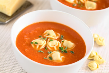 Homemade fresh cream of tomato soup with tortellini garnished with fresh oregano leaves, photographed with natural light (Selective Focus, Focus in the middle of the first soup)