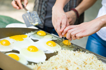 Young Adult Couple Cracking Open and Cooking Eggs and Potatoes At The Campground