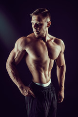 bodybuilder posing in studio on dark bakground. Beautiful sporty guy male power. Fitness muscled man
