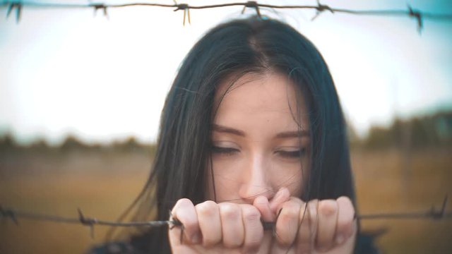 girl brunette refugee behind barbed wire camp slow motion video lifestyle. the concept of freedom is upset Woman hands and barbed wire. girl Refugee, prison, refugees captivity concept