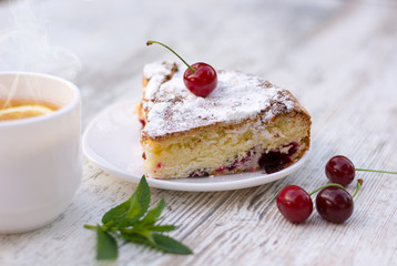 Вкусный кусок вишневого пирога на белой тарелке и белая чашка горячего чая с лимоном и мятой. Крупный план. Мокап.