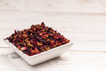 Close-up view of dry brown tea leaves with particles of fruits and flowers in small white ceramic plate on white table