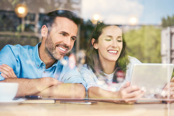 Cheerful couple using tablet while sitting in cafe and having coffee