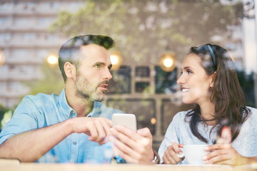 Couple talking and using smartphone while having coffee in cafe