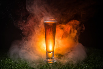 Creative concept. Single beer glass on green grass at dark toned foggy background. Watch football (soccer) with beer concept.