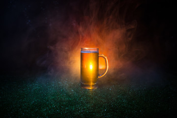 Creative concept. Single beer glass on green grass at dark toned foggy background. Watch football (soccer) with beer concept.