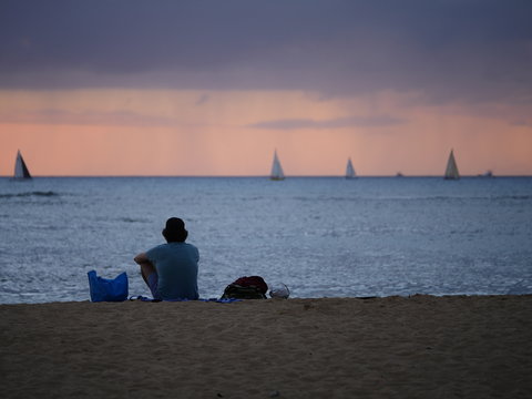 A Person Sitting Alone On The Beach Watching The Sunset And Sailboats 