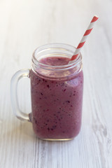 Mason jar mug with smoothie on a white wooden table, side view.